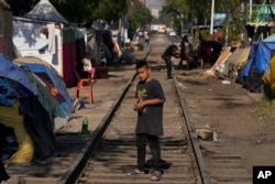 Joven migrante juega en las vías del tren bordeadas por tiendas de campaña y refugios improvisados en Ciudad de México, el martes 26 de marzo de 2024. (AP Photo/Fernando Llano)