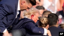 El candidato presidencial republicano, el expresidente Donald Trump, recibe ayuda para bajar del escenario en un evento de campaña en Butler, Pensilvania, el sábado 13 de julio de 2024. (Foto AP/Gene J. Puskar)