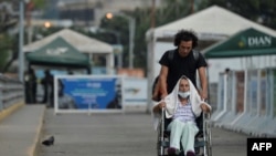 Steve Oliveros conduce a su madre en silla de ruedas de vuelta a Colombia tras serle negado el paso en la frontera para entrar a Venezuela. 