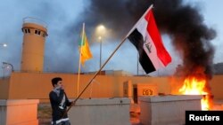 Un manifestante sostiene una bandera iraquí durante una protesta para condenar los ataques aéreos en bases de Hashd al-Shaabi (fuerzas paramilitares), frente a la puerta principal de la embajada de EEUU en Bagdad.