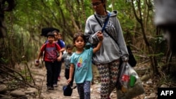 Una mujer camina con sus hijos a través del río Táchira, por las trochas que conectan a Venezuela con Colombia. 