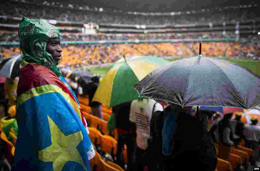 Un sudafricano se envuelve en una bandera para protegerse de la intensa lluvia caída durante el multitudinario servicio religioso oficial celebrado en honor del expresidente sudafricano Nelson Mandela.