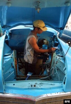 Un hombre pinta el interior de la carrocería de un viejo auto de fabricación norteamericana.