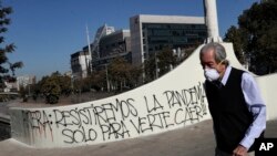 Un hombre que usa una mascarilla pasa junto a un graffiti contra el presidente chileno Sebastián Piñera en medio de la pandemia del coronavirus, en Santiago de Chile. (AP/Esteban Félix)