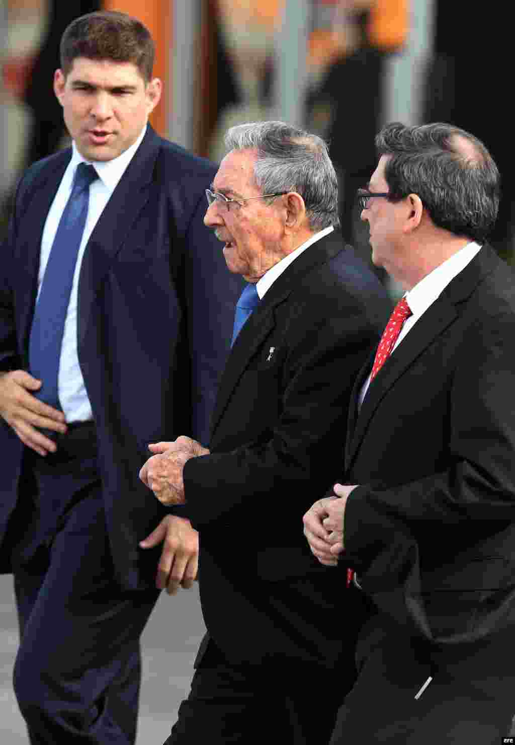 El nieto-escolta de Raúl Castro (i), Raúl Castro (c) y el canciller cubano Bruno Rodríguez en el recibimiento al Patriarca ruso. 