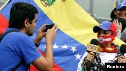 Un hombre toma una foto de una mujer que lleva una mordaza y una cadena mientras sostiene micrófonos durante una manifestación para conmemorar el Día Mundial de la Libertad de Prensa en Caracas, el 3 de mayo de 2016.