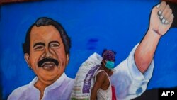 Un indigente pasa protegiéndose ocntra el coronavirus frente a un cartel de mandatario de Nicaragua, Daniel Ortega.