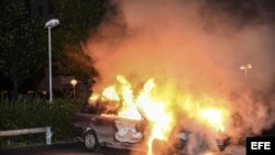  Vista de un vehículo en llamas tras los disturbios registrados en el barrio de Kista, en Estocolmo, Suecia, en la madrugada de hoy miércoles 22 de mayo de 2013.