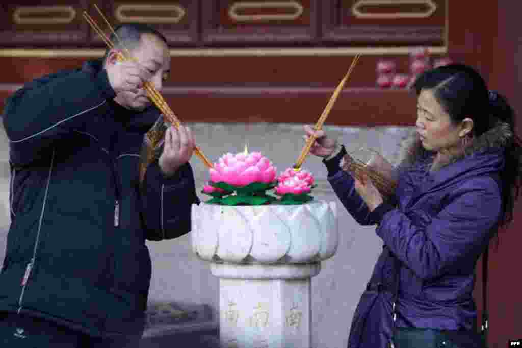 Un par de fieles chinos queman varas de incienso en un templo para celebrar la llegada del nuevo año en la ciudad de Qingdao, en la provincia oriental china de Shandong.