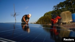 Denis Tamayo, de 30 años, y Alejandro Guerra, de 30, instalan un panel solar en la azotea de un edificio residencial en La Habana, Cuba, 16 de febrero de 2026. REUTERS/Norlys Perez