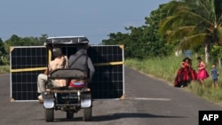 Cubanos transportan un panel solar en un triciclo por una carretera en la provincia de Pinar del Río, el 26 de julio de 2026. (Foto de YAMIL LAGE / AFP)