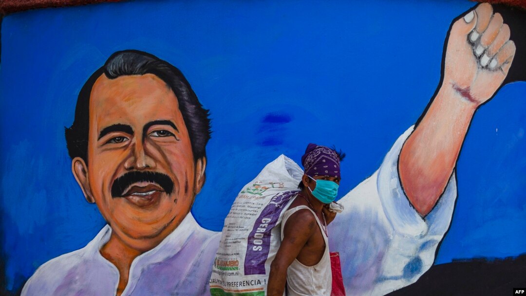 Un indigente pasa protegiéndose ocntra el coronavirus frente a un cartel de mandatario de Nicaragua, Daniel Ortega.