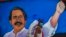 Un indigente pasa protegiéndose ocntra el coronavirus frente a un cartel de mandatario de Nicaragua, Daniel Ortega.