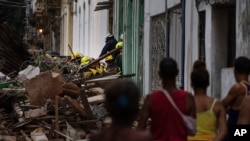 La gente observa a los bomberos limpiando los escombros de un edificio que se derrumbó parcialmente en busca de sobrevivientes en La Habana, Cuba, el 4 de octubre de 2023. (Foto AP/Ramon Espinosa)
