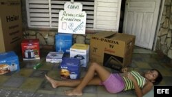ARCHIVO. Una joven descansa en el portal de su casa que donde se muestran algunas cajas de los efectos electrodomésticos de la llamada "revolución energética" en Cuba. 