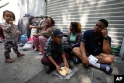 Familia migrante desayuna junto a las vías del tren en Ciudad de México, el martes 26 de marzo de 2024. (AP Photo/Fernando Llano)