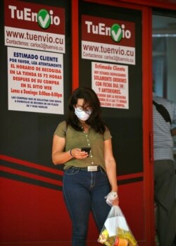 Una mujer chequea su teléfono frente a un centro de recogida de compras online en La Habana, un servicio que resultó desastroso por la falta de infraestructura. (YAMIL LAGE / AFP)