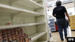 Un cliente recorre un pasillo con estanterías desabastecidas en un supermercado.