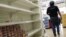 Un cliente recorre un pasillo con estanterías desabastecidas en un supermercado.