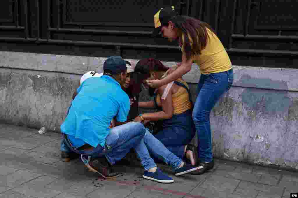 Un grupo de personas ayuda a una mujer durante un enfrentamiento entre un grupo de personas adeptas al oficialismo y personas opositoras.
