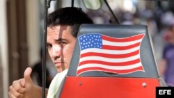 Un hombre saluda desde una bicitaxi con la bandera de EEUU.