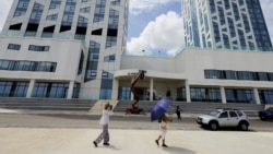 Una mujer toma una fotografía mientras camina frente al hotel donde unos trabajadores retiran de la fachada el nombre de la marca "Aston" —perteneciente a la cadena hotelera Archipelago International.