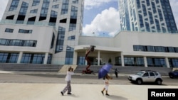 Una mujer toma una fotografía mientras camina frente al hotel donde unos trabajadores retiran de la fachada el nombre de la marca "Aston" —perteneciente a la cadena hotelera Archipelago International.