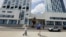 Una mujer toma una fotografía mientras camina frente al hotel donde unos trabajadores retiran de la fachada el nombre de la marca "Aston" —perteneciente a la cadena hotelera Archipelago International.