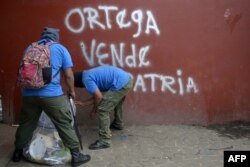 Paramilitares limpian el piso cerca de un grafiti que reza: "Ortega, vende patria", en Monimbo, Masaya.
