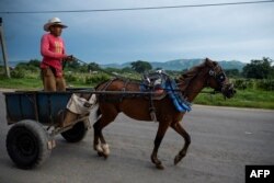 Un hombre viaja en su carro tirado por caballos por una carretera en Santiago de Cuba, en el este de Cuba, el 24 de septiembre de 2023. (Foto de Yamil LAGE / AFP)
