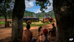 En esta fotografía del 24 de agosto de 2019, una familia sentada en la sombra observa un tractor con una piscina rodante en el vecindario de El Infernal, en la provincia de Pinar del Río, Cuba. (AP Foto/Ramon Espinosa)