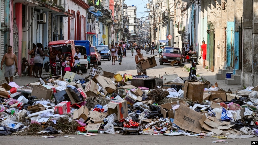 Una mujer sostiene una caja de cartón frente a basura acumulada en una calle de La Habana el 19 de junio de 2026. (Foto de YAMIL LAGE / AFP)