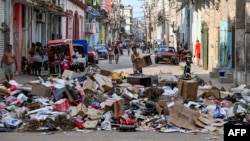 Una mujer sostiene una caja de cartón frente a basura acumulada en una calle de La Habana el 19 de junio de 2026. (Foto de YAMIL LAGE / AFP)