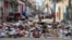 Una mujer sostiene una caja de cartón frente a basura acumulada en una calle de La Habana el 19 de junio de 2026. (Foto de YAMIL LAGE / AFP)