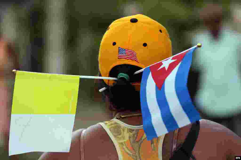 Las banderas del Vaticano y Cuba, más la de EEUU en la gorra de una cubana que espera al Papa. 