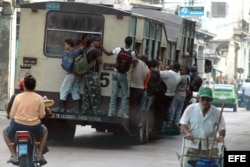 Varias personas viajan colgando de un ómnibus, popularmente conocido como camello