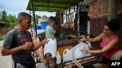 A Cuban carrying plastic drums and buckets with water on a horse-drawn cart fills bottles with water in Havana, Cuba, on September 24, 2024.