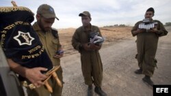 Soldado israelíes cargan con una Torá y libros de rezo mientras otros soldados se preparan para desplegarse junto a la frontera con Gaza, en Israel. 
