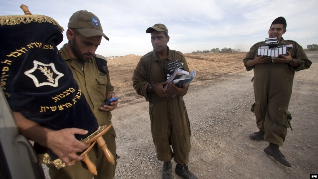 Soldado israelíes cargan con una Torá y libros de rezo mientras otros soldados se preparan para desplegarse junto a la frontera con Gaza, en Israel. 