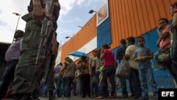 Un grupo de personas aguardan afuera del supermercado Día a Día para ingresar y hacer compras, bajo presencia militar, en la ciudad de Caracas (Venezuela). 