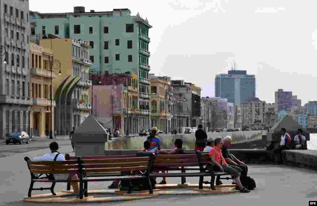 Varias personas se sientan en los bancos que conforman la obra "Bancontodos", del artista cubano Inti Hernández", colocada en el malecón de La Habana (Cuba) como parte de la XI Bienal de La Habana 