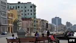 Varias personas se sientan en los bancos que conforman la obra "Bancontodos", del artista cubano Inti Hernández", colocada en el Malecón de La Habana.