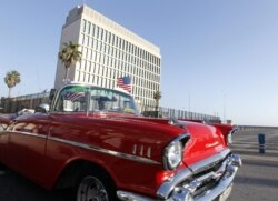 Un auto clásico pasa con una bandera de Estados Unidos frente a la embajada de ese país en La Habana.