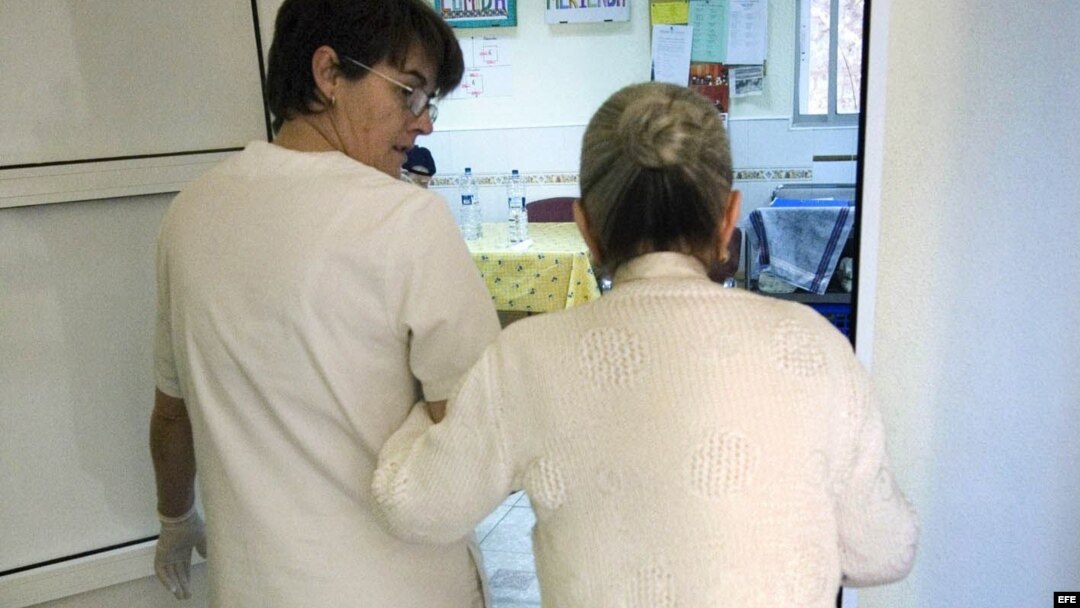 Una auxiliar acompaña al comedor a una enferma de alzheimer en el centro de día "La Pineda" en Castellón. 