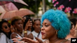 Una mujer de cabello azul lanza un beso al público mientras camina por la pasarela en un desfile de moda de peinados afro en La Habana, Cuba, el sábado 31 de agosto de 2024. (Foto AP/Ramon Espinosa)