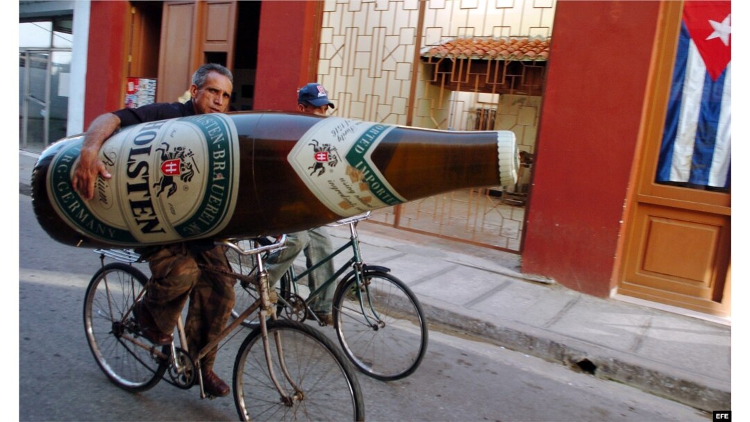 Un hombre se traslada en bicicleta con una botella de cerveza inflable..