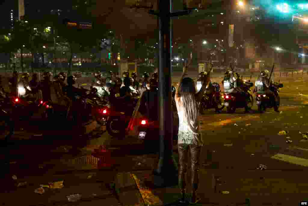 Una mujer hace un llamado a la paz mientras protestantes se enfrentan con miembros de la Guardia Nacional Bolivariana (GNB)