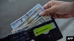 Un hombre muestra su billetera con dólares estadounidenses y pesos cubanos en una calle de La Habana. (YAMIL LAGE/AFP)