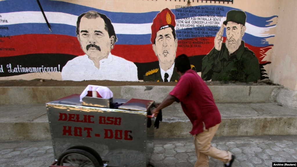 Un vendedor ambulante empuja su carrito junto a un mural con las imágenes de los fallecidos gobernantes Hugo Chávez (C), de Venezuela, y Fidel Castro, de Cuba, junto al presidente de Nicaragua, Daniel Ortega.