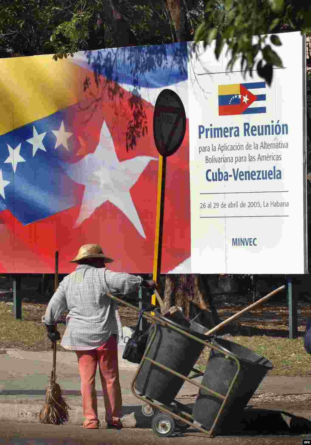 Una mujer barre la calle frente a un cartel del ALBA.